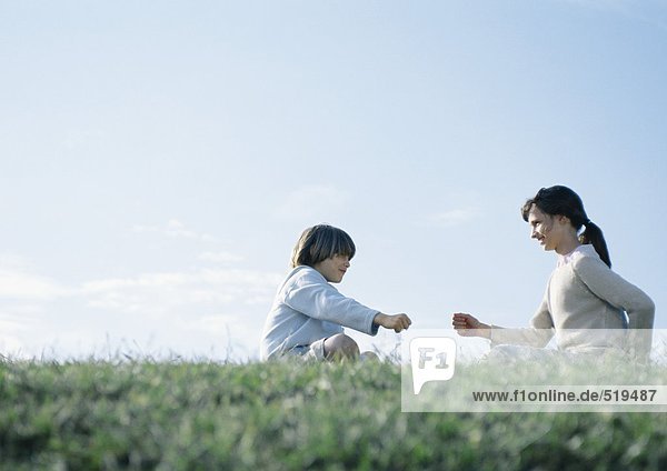 Junge und Mädchen sitzen auf Gras und spielen eine Steinschere.