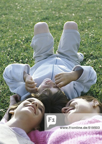 Mutter auf Gras liegend mit Junge und Mädchen  Kopf an Kopf