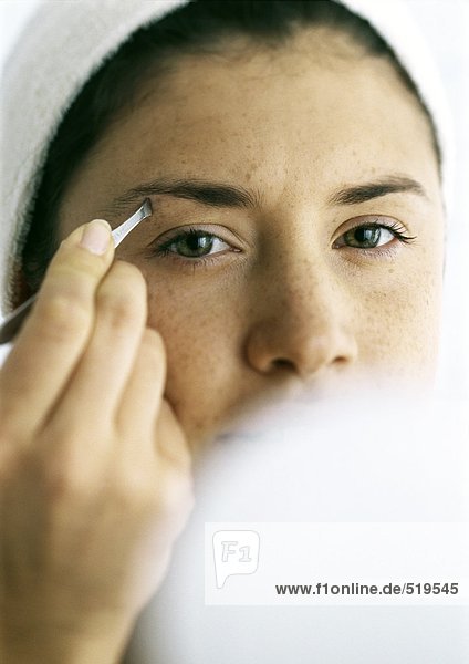 Junge Frau zupft die Augenbrauen  kompakt verschwommen im Vordergrund