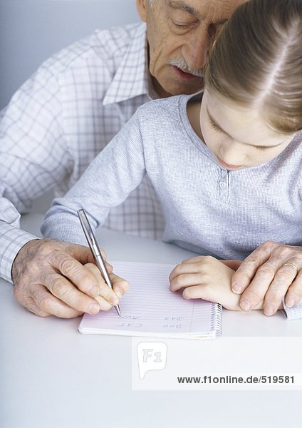 Grandfather helping granddaughter write in notebook