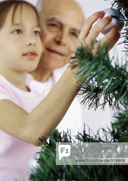 Mädchen und Großvater schmücken Weihnachtsbaum