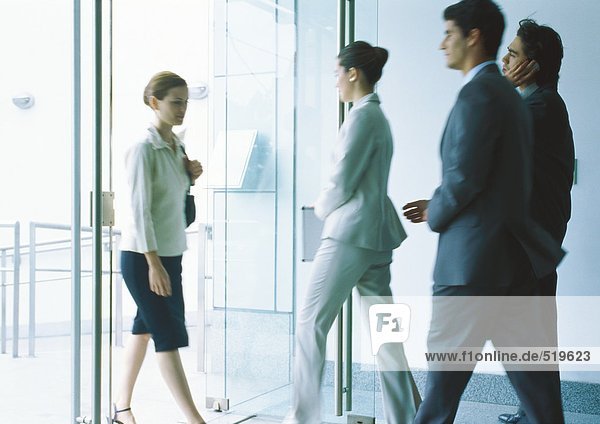 Businesspeople entering and exiting through glass doors