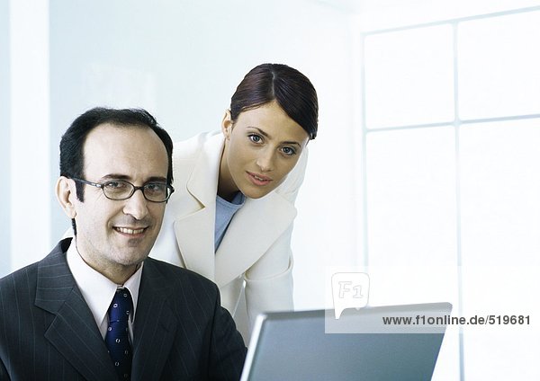 Businessman and businesswoman with laptop looking at camera