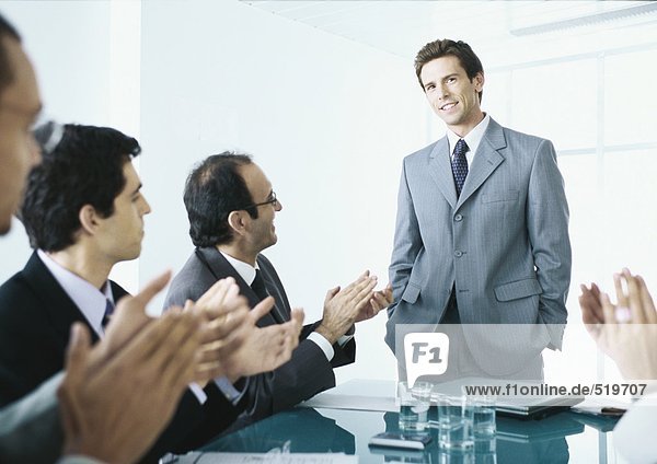 Seated businesspeople applauding businessman standing at end of table