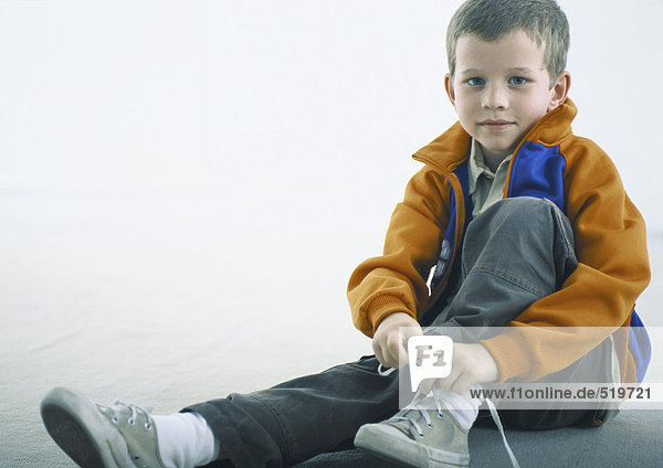 Junge sitzt auf dem Boden  Schnürschuh