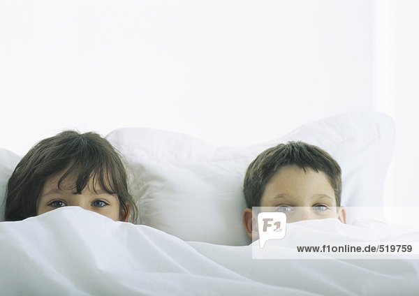 Boy and girl lying in bed  faces partially covered by duvet