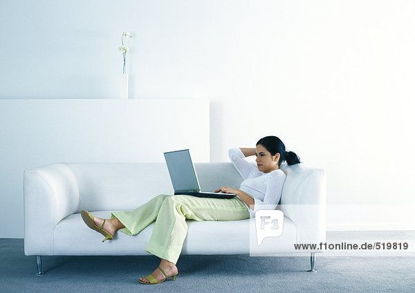 Woman lounging on sofa and using laptop