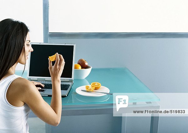 Frau am Tisch sitzend mit Laptop  Obst essend