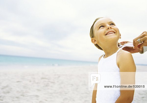 Mädchen steht am Strand  während Mutter das Hemd bindet.