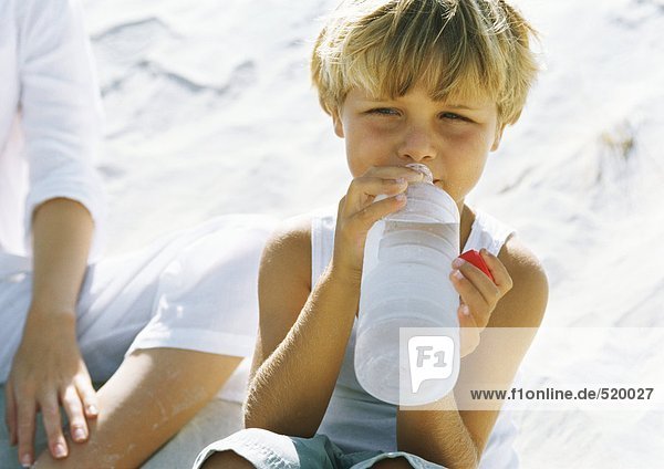 Junge sitzend auf Sand neben Mutter  Trinkwasser