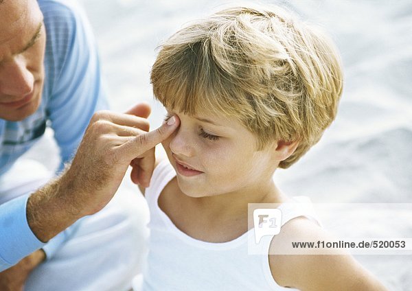 Vater berührt das Gesicht des Jungen mit einem Finger am Strand