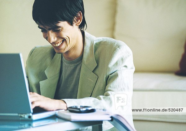 Junger Mann lächelnd  mit Laptop auf Couchtisch