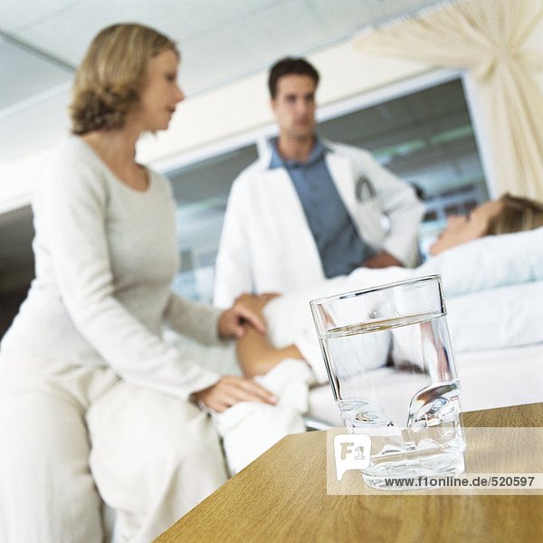 Glass of water on table and patient receiving visit from male doctor and woman