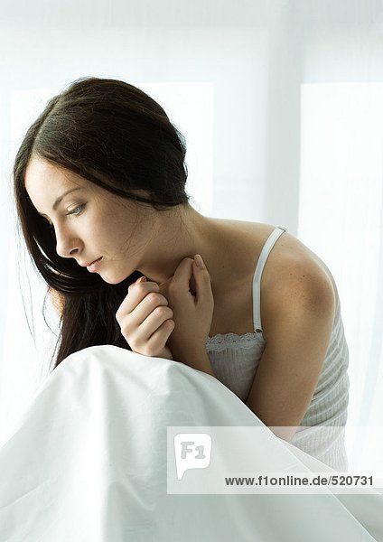 Junge Frau im Bett sitzend  zusammengerollt