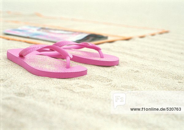Rosa Flipflops neben der Strandmatte am Strand