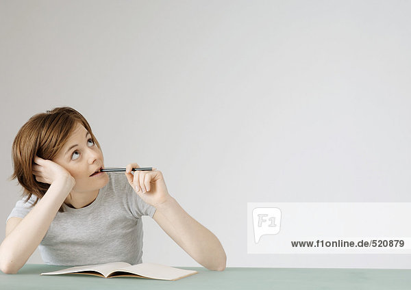 Junge Frau sitzend mit geöffnetem Notizbuch  hält Bleistift an den Mund