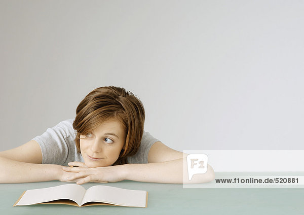 Junge Frau sitzend mit Kopf auf Tisch neben offenem Notizbuch