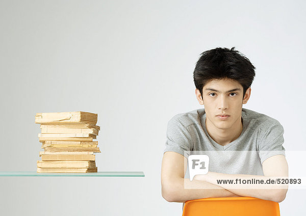Junger Mann sitzt neben einem Bücherstapel  Porträt