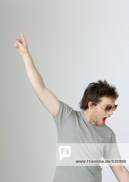 Junger Mann mit erhobener Hand in der Luft und offenem Mund, mit Sonnenbrille, Portrait