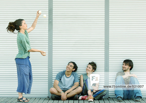 Junge Frau jongliert  während Freunde auf dem Boden sitzen und zusehen.