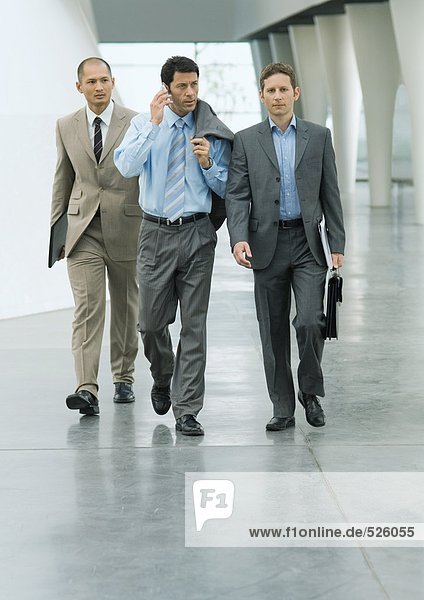 Drei Geschäftsleute gehen durch die Lobby  einer per Handy