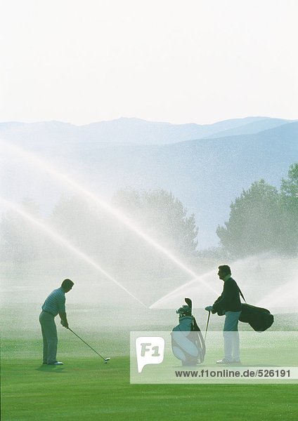 Golfers golfing among sprinklers