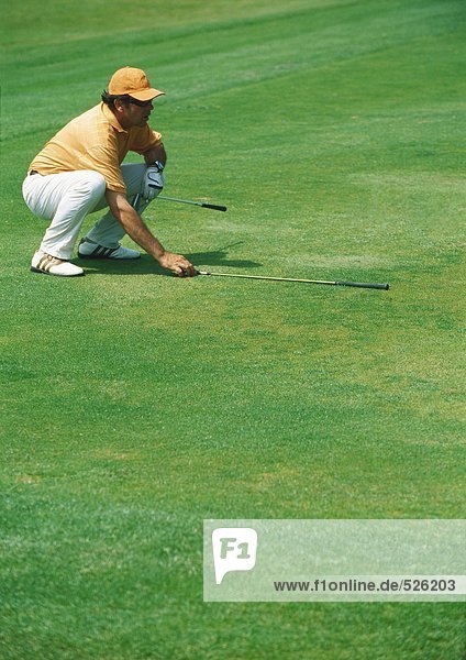 Golfer crouching on green  pointing golf club