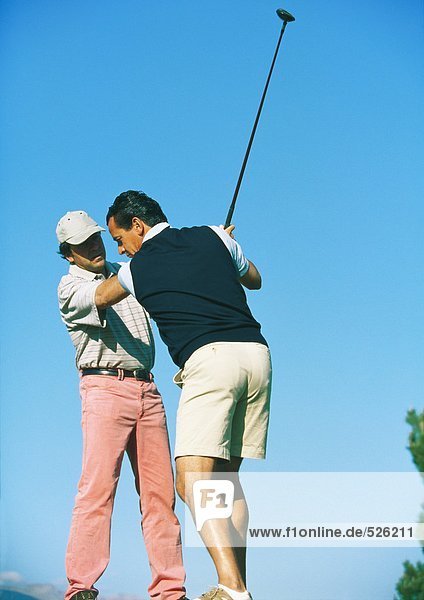 Mann nimmt Unterricht bei einem Golflehrer
