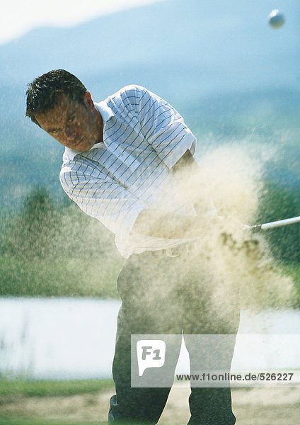 Golfer  mid-swing in sand trap  with sand in mid-air
