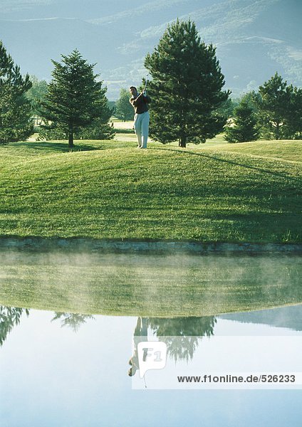 Golfer swinging near pond
