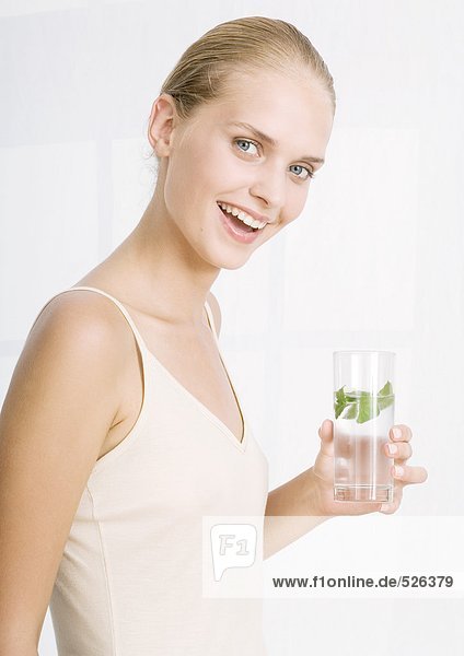 Frau lächelt und hält ein Glas Kräuterwasser in der Hand