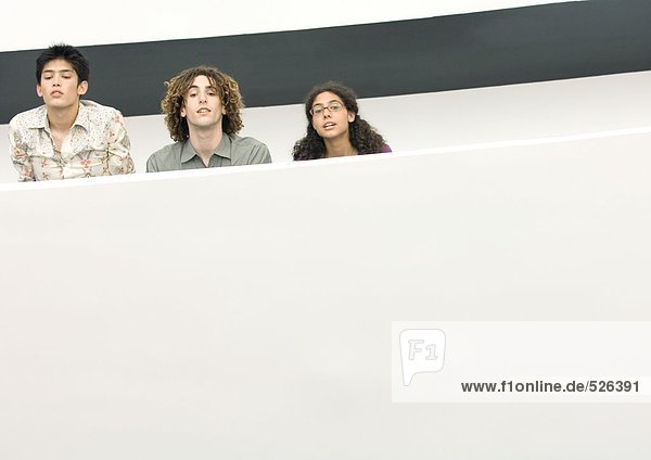Drei junge Leute schauen über den Balkonrand