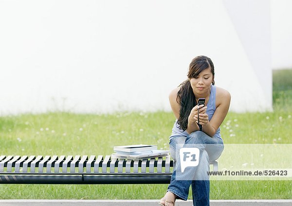 Junge Frau sitzt am Ende der Bank und schaut auf das Handy