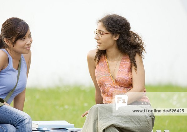 Zwei junge Frauen  die zusammen auf der Bank sitzen und reden.