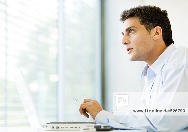 Mann am Laptop sitzend  aus dem Fenster schauend
