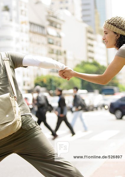 Ein junges Paar hält sich an den Händen und rennt über die Straße.