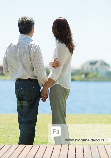 Couple standing and looking at lake  holding hands
