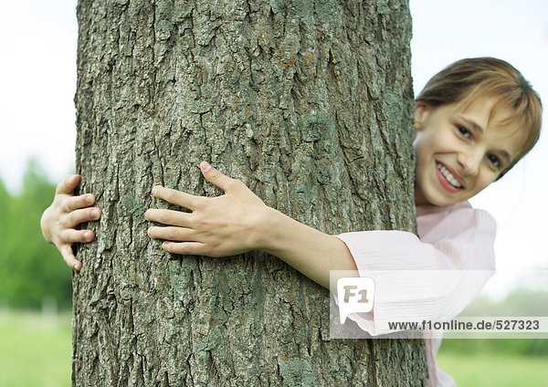 Mädchen umarmen Baum und lächeln