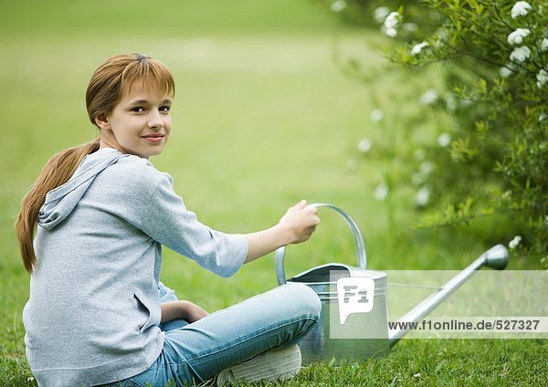Mädchen auf Gras sitzend mit Gießkanne