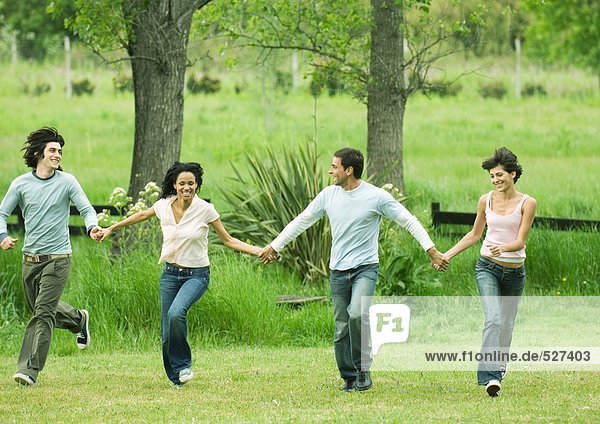 Four young friends holding hands and skipping in field