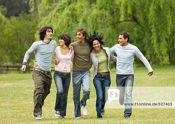 Group of young friends with arms around each other  skipping across field