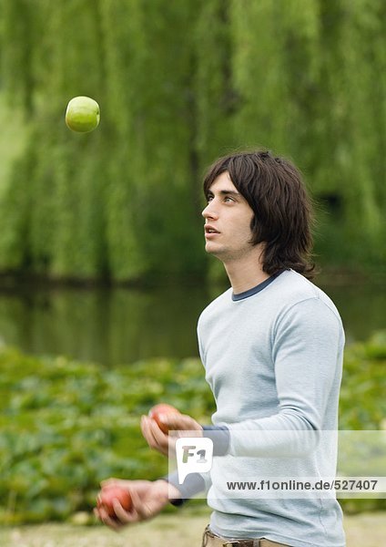 Ein junger Mann jongliert mit Äpfeln im Freien.