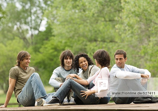 Gruppe junger erwachsener Freunde,  die zusammen draußen sitzen.