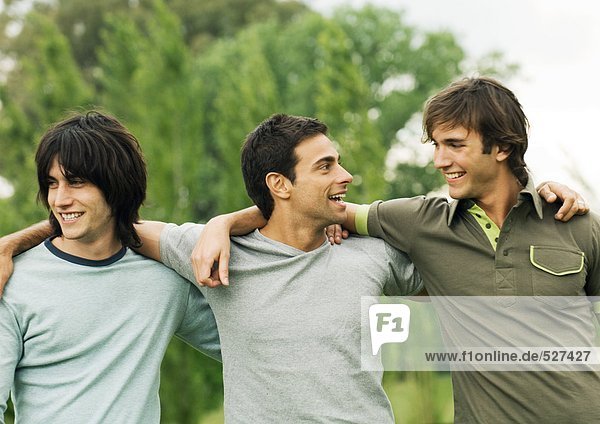 Three young male friends with arms around each other's shoulders