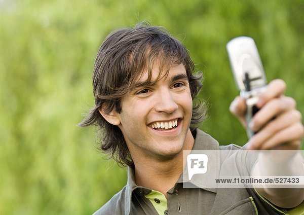 Junger Mann hält Handy hoch und lächelt