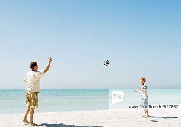 Vater und Sohn werfen Ball am Strand
