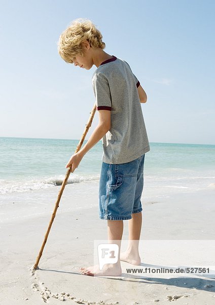 Jungenzeichnung mit Stock auf Sand