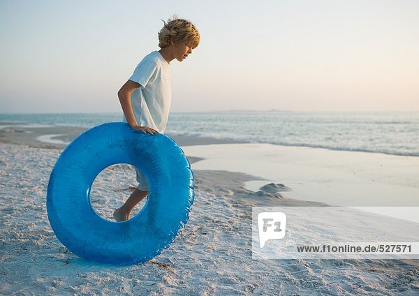 Junge rollt Schlauch am Strand in Richtung Wasser