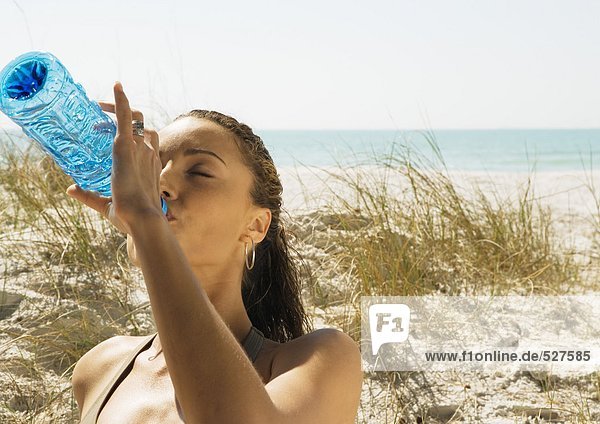 Frau trinkt Wasser in Flaschen am Strand