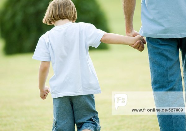 Boy walking next to father  holding his hand  rear view